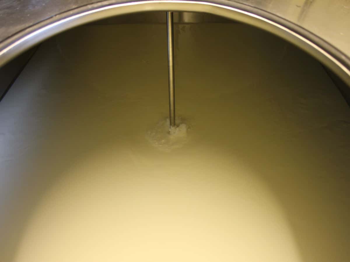 Ein Blick in einen Milchtank, man sieht die cremegelbe Milch und das Rührwerk im Edelstahltank.